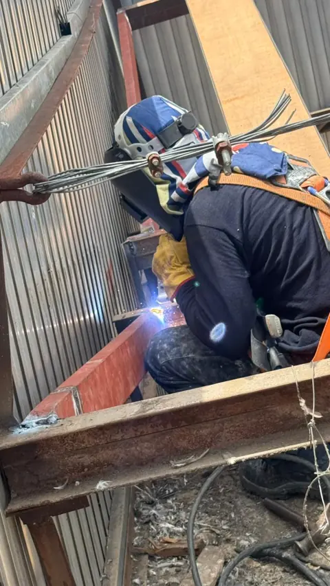 Soldador con arnés uniendo vigas metálicas de la cubierta